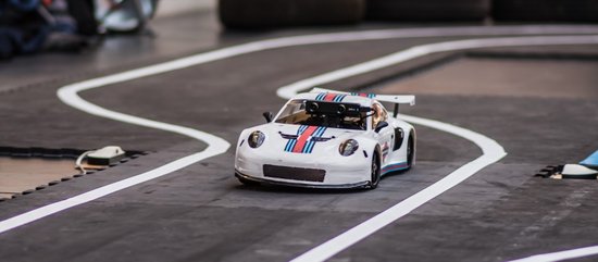 Autonomous model car in white color with blue-red stripes in the middle on the built-up racetrack in the foyer of the Munich University of Applied Sciences